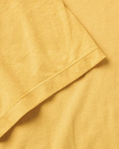 Close-up detail of Taylor Stitch Cotton Hemp Tee sleeve hem showing stitching and soft organic cotton fabric texture in Goldfinch yellow