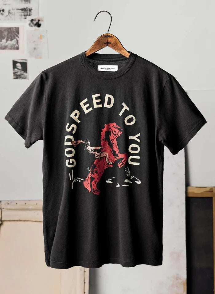 The Godspeed Tee by Imogene + Willie on a wooden hanger in a studio setting, showing the full front with a screen-printed graphic of a rearing red horse with rider and the text 'GODSPEED TO YOU' in cream arched lettering on a black cotton tee