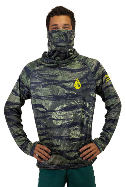 Male model wearing the Waihana Tropicam Sun Shirt in green camouflage with built-in neck gaiter pulled up over his face, yellow Waihana brand mark on chest, hands on hips against a white background.