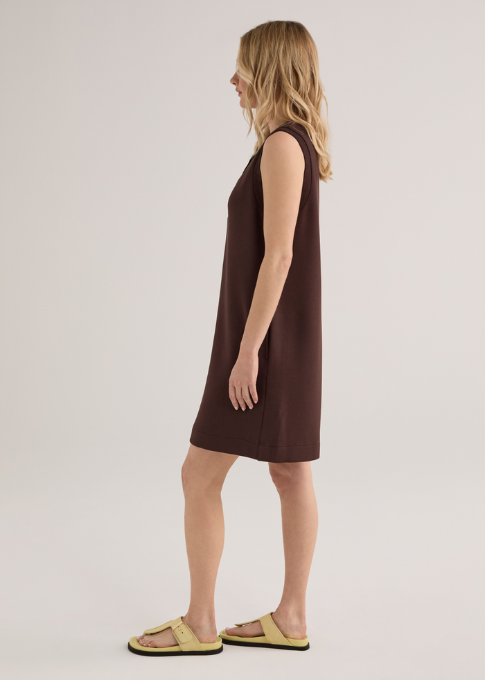 Woman turned to the side wearing a brown sleeveless mini dress with yellow sandals