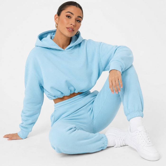 Women's blue hoodie and jogger set shown on a female model in a seated studio pose against a clean white background.