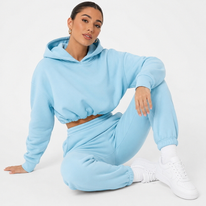 Women's blue hoodie and jogger set shown on a female model in a seated studio pose against a clean white background.